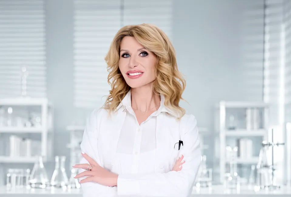 Dr Ivy Skincare founder with blonde hair wearing a white laboratory coat, standing in a modern skincare laboratory surrounded by cosmetic products.